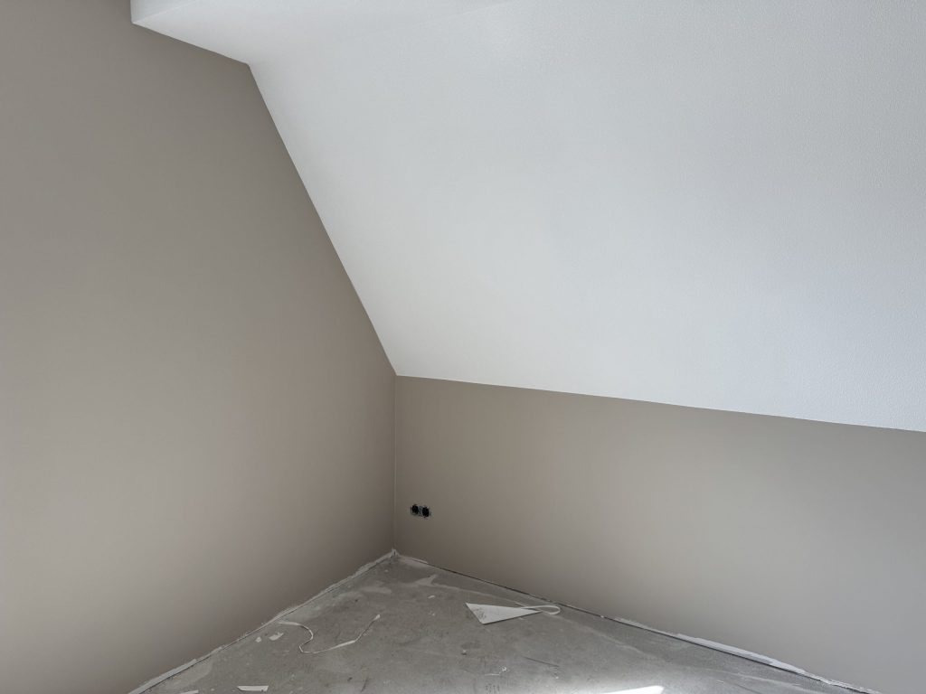 Zolderkamer met een schuine wand, egaal beige gesausde muren en een wit plafond